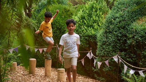 Two young boys walking between hedges through the garden in summer at Nymans, West Sussex